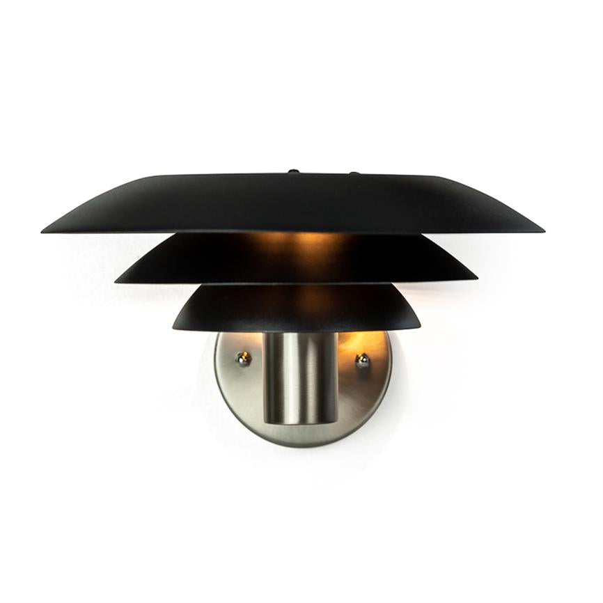 Væglampe med tre sorte, skålformede skærme; den udsender varm opadrettet belysning fra et børstet stålbeslag monteret på en hvid væg.