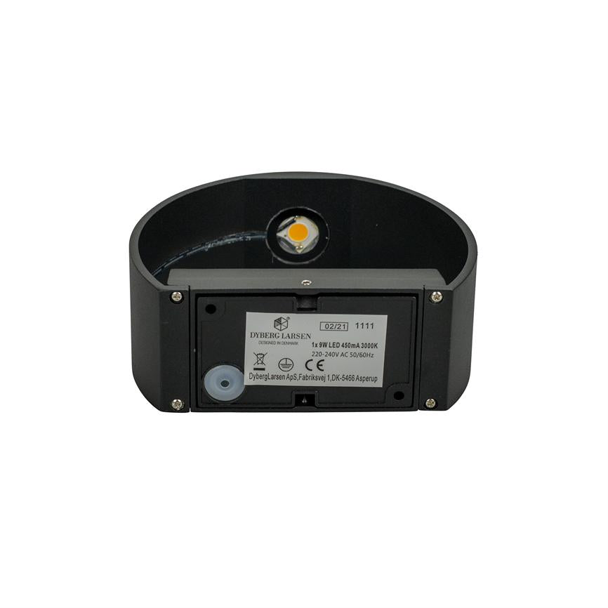 Sort oval væglampe viser åben bagside med synligt LED-modul og monteringsmærkat, placeret mod hvid baggrund.
 
 Transkriberet tekst:
 DYBERG LARSEN
 DESIGNED IN DENMARK
 02/21 1111
 1x 9W LED 450mA 3000K
 220-240V AC 50/60Hz
 CE
 DybergLarsen ApS, Fabriksvej 1, DK-5466 Asperup
