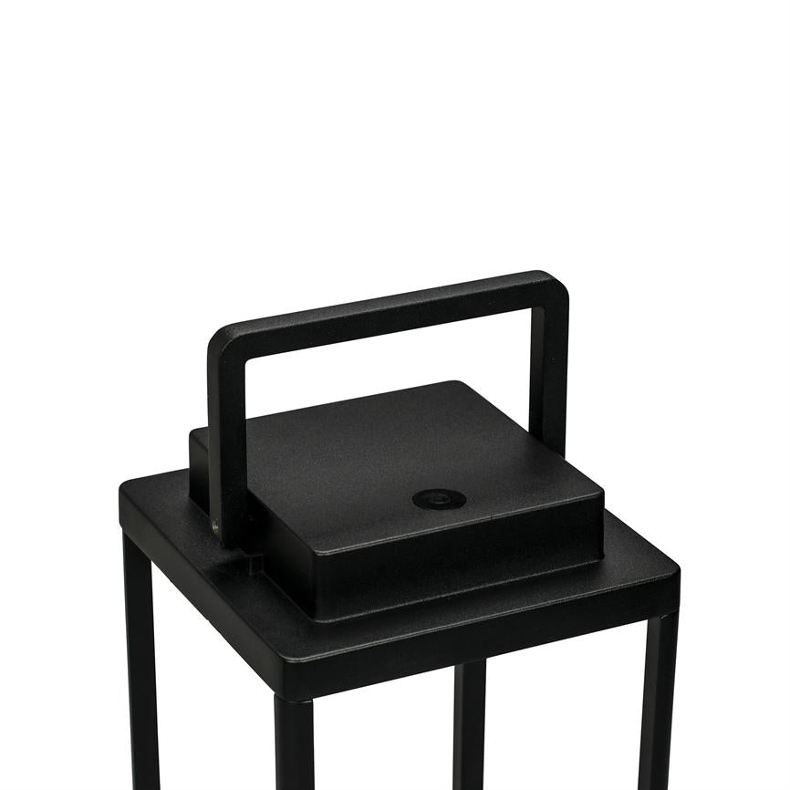 Sort, firkantet metal lanterne med rektangulært opretstående håndtag, placeret på slanke ben; toppen viser en lille rund knap, fotograferet mod ensartet hvid baggrund.