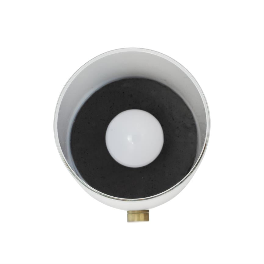 En hvid lyskilde (pære) sidder centreret i en cirkulær, sølvfarvet metal-skærm med mørk inderside; lille messingknap ses nederst, mod en hvid baggrund.