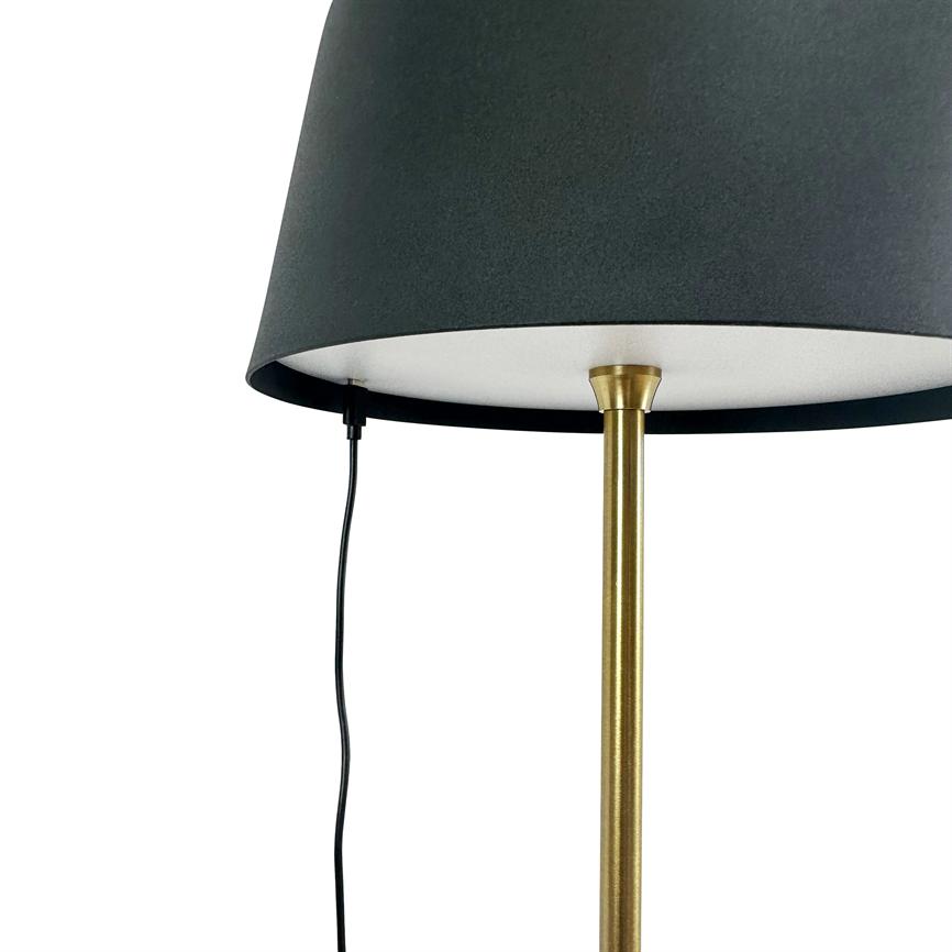 En guldfarvet lampestang holder en sort cylindrisk lampeskærm; en sort strømkabel hænger ned fra skærmens underside mod en ren, hvid baggrund.