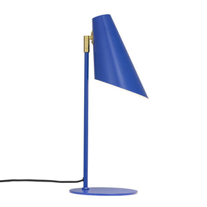 En blå bordlampe med skråtstillet, konisk skærm hælder fremad; skærmen er monteret på en tynd lodret stang med rund fod, sort strømledning ligger mod hvid baggrund.