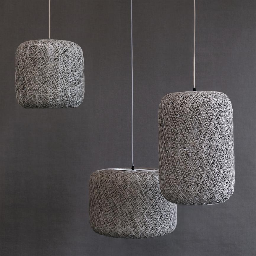Tre hængende lamper af flettet snor svæver i forskellige højder foran en ensartet grå væg, med cylinder- og kubeformede skærme ophængt i tynde hvide ledninger.