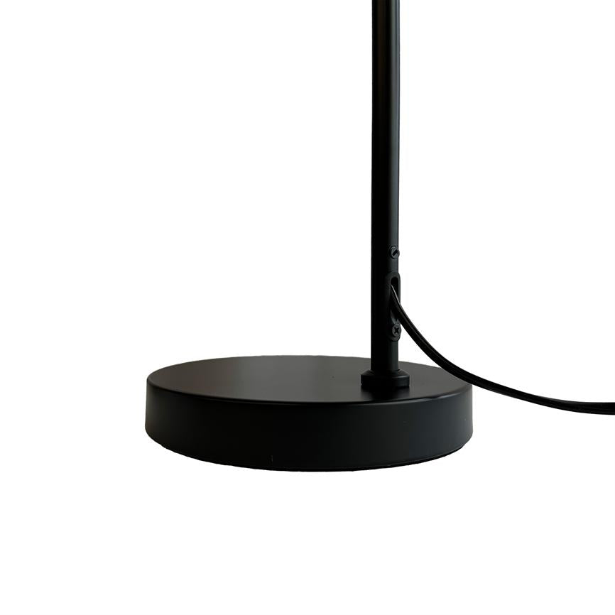 Sort, rund lampefod holder en tynd lodret stang; en sort ledning fører ud gennem stangen og buer mod højre, alt på en ren hvid baggrund.