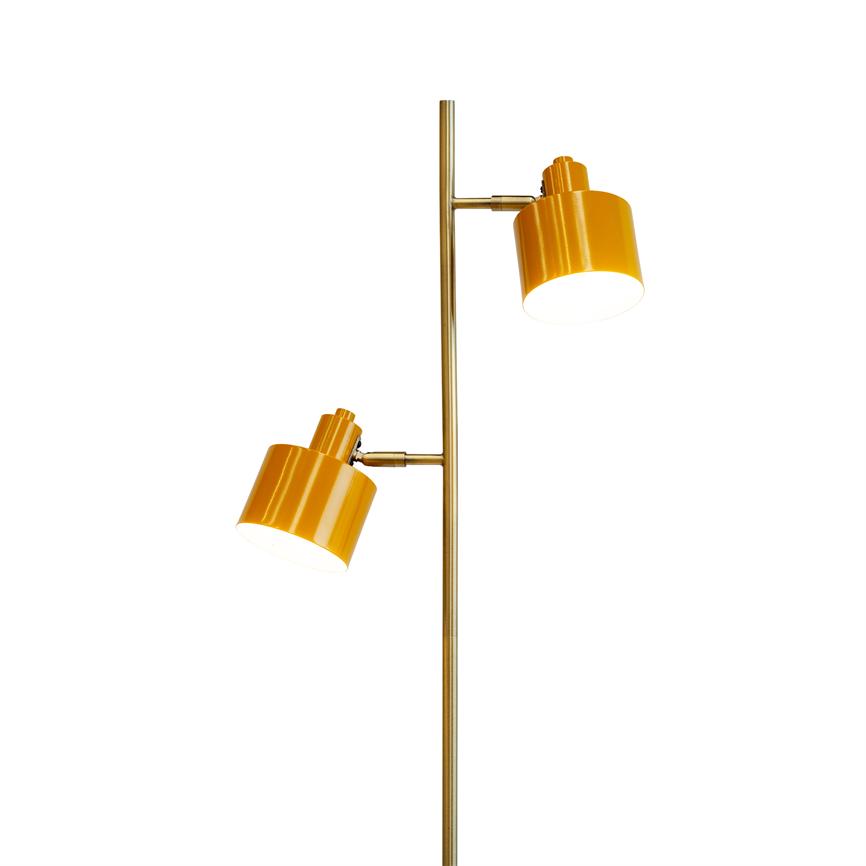 Gulvlampe med to gule, justerbare skærme monteret på en slank, messingfarvet stolpe; skærmene peger nedad og kaster lys mod en hvid baggrund.