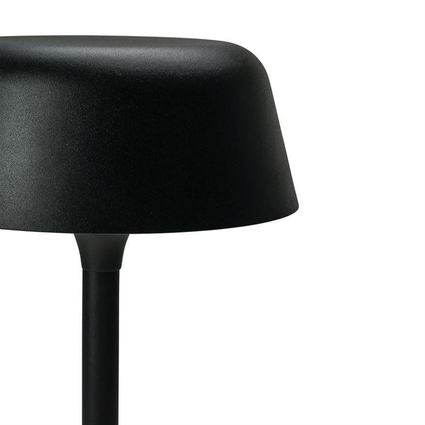 Sort bordlampe står med en kuppelformet skærm på en slank stang; delvist beskåret til højre mod en ren, hvid baggrund.