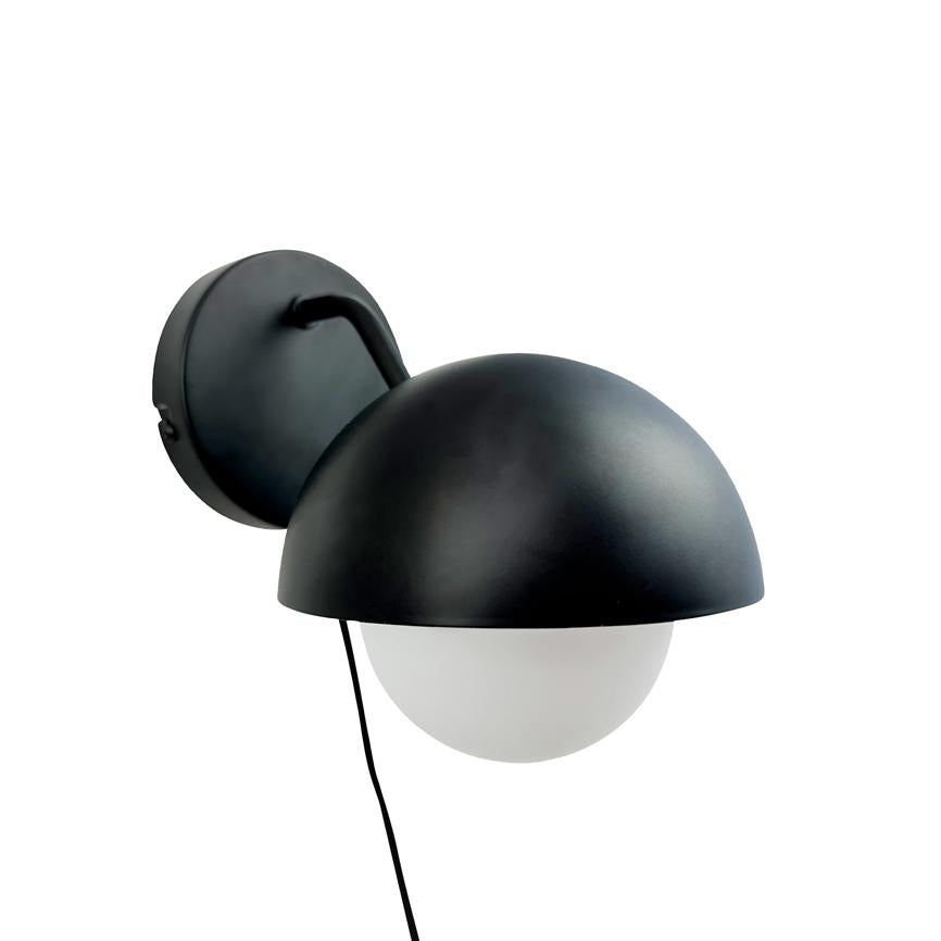Væglampe med sort, halvkugleformet skærm og hvid, matteret glaskugle under; hænger monteret på rundt sort vægbeslag med sort ledning nedad; neutral hvid baggrund.