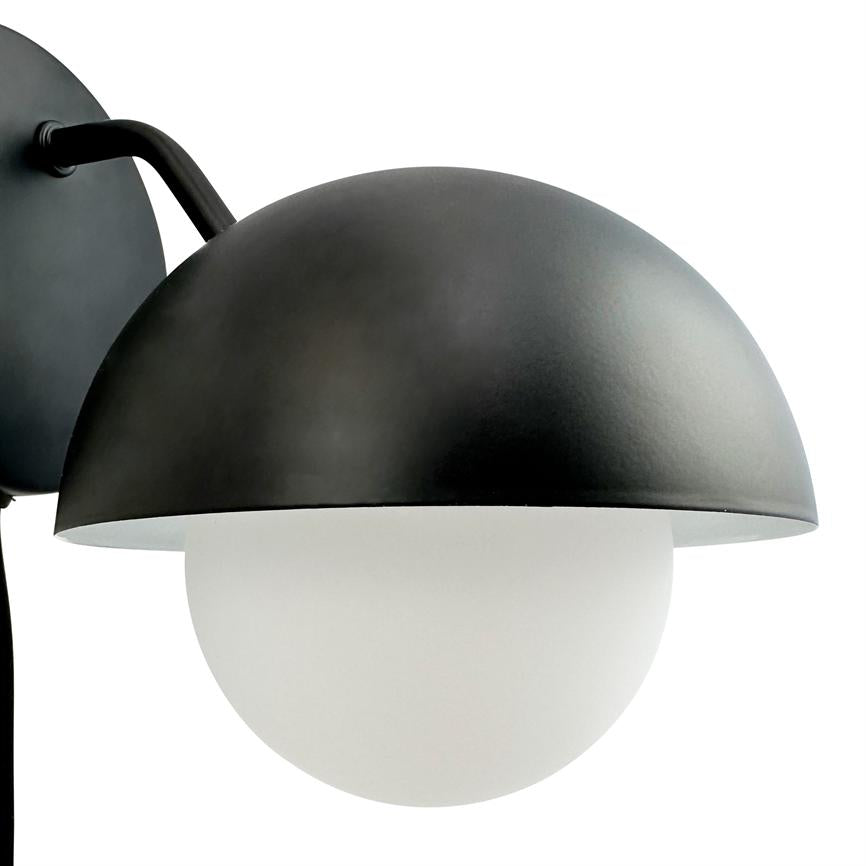 Væglampe med sort halvkugleskærm, som omslutter en hvid opalglas-kugle; sort arm og rundt vægbeslag monteret mod en neutral hvid baggrund.