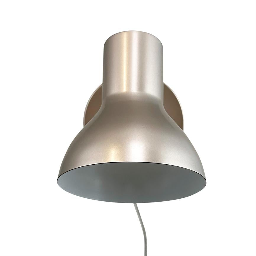 Væglampe i børstet sølvmetal peger nedad; den har rund kuppel og cylindrisk hals, er monteret på en cirkulær vægplade med hvid ledning hængende mod en neutral hvid baggrund.