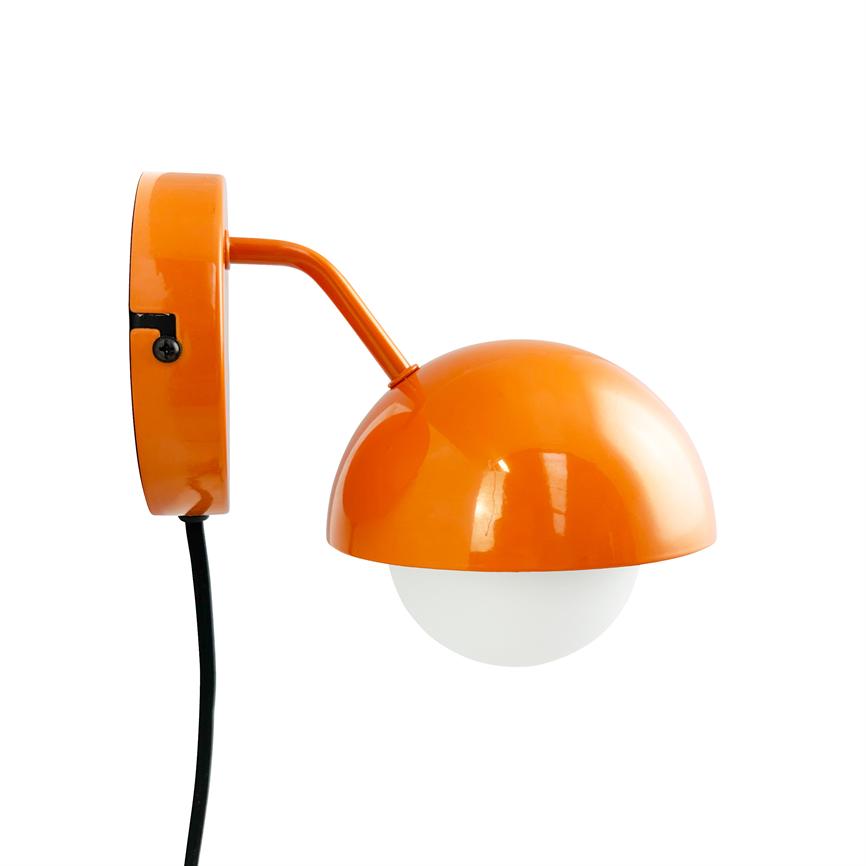 Væglampe med orange halvkugleskærm, arm bøjet mod højre og hvid rund pære nedenunder, fastgjort til rundt vægbeslag; sort ledning hænger ned mod hvid baggrund.