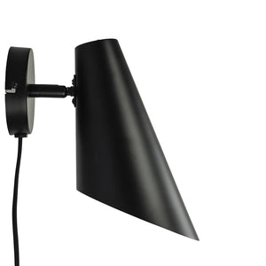 Sort mat metal væglampe med spids, skråtstående skærm; monteret på rundt vægbeslag, kabel hænger ned, skærmen er vinklet nedad mod hvid baggrund.
