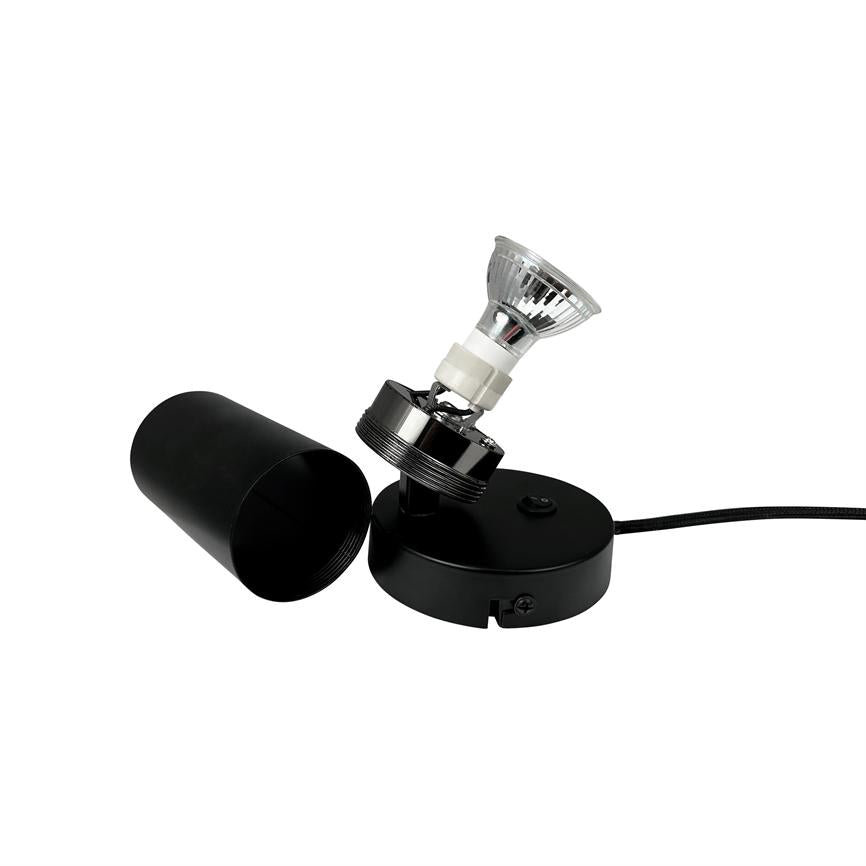 Sort lampefod med rund base og afmonteret cylinder-skygge; en GU10-spotpære sidder i en vipbar fatning, skyggen ligger ved siden af, alt placeret på hvid baggrund.