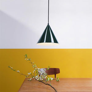 En grøn kegleformet pendel hænger over et træbord. En blomstrende gren ligger på bordet foran en brun træstol, foran en væg malet hvid øverst og varm gul nederst.