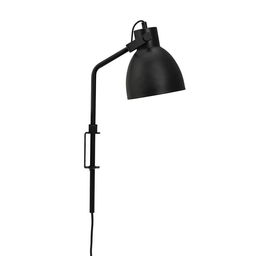 Sort metal væglampe med buet arm, skærm vinklet nedad; lampen er fastgjort med en klemme på en lodret stang og ses mod en neutral, hvid baggrund.