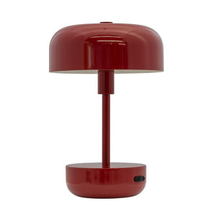 Rød bordlampe står centralt med rund skærm over en slank stolpe og rund fod med sort tænd/sluk-knap; minimalistisk design på en neutral hvid baggrund.
