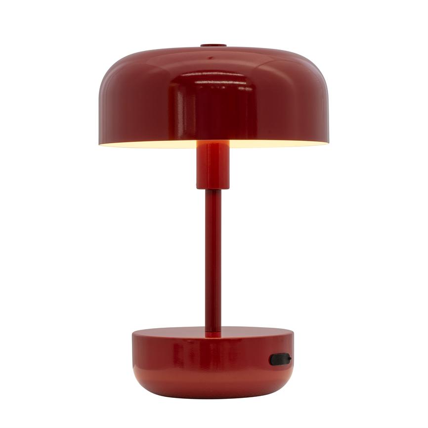 Bordlampe i rød, moderne design; tændt og kaster varmt, nedadrettet lys; cylindrisk stilk forbinder rund base og kuppelskærm; placeret mod neutral, hvid baggrund.