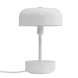 Hvid rund bordlampe står på en enkel rund fod; en tynd søjle bærer en halvkugleformet skærm, afbildet mod en ensartet hvid baggrund med synlig ledning.
