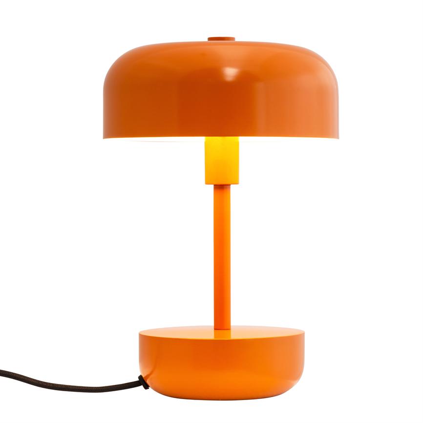 Orange bordlampe står tændt med rund kuppelskærm over en smal central skaft og rund base; den afgiver varmt lys mod en ensartet hvid baggrund, med sort tekstilledning til venstre.