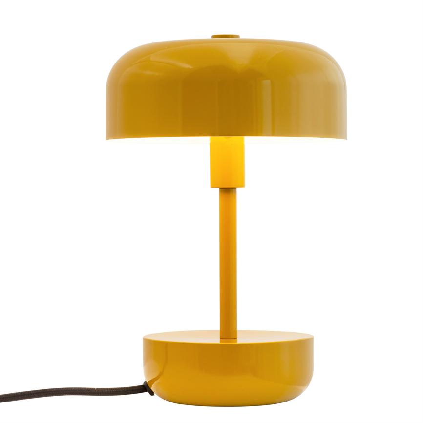 Gul bordlampe med kupelformet skærm, lodret skaft og rund fod; lampen er tændt, kaster lys nedad og har en synlig sort ledning mod en hvid studiobaggrund.