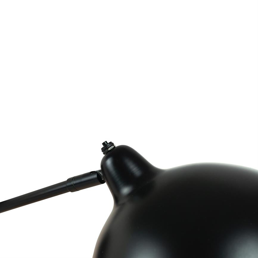 Sort metal lampeskærm, fastgjort til en smal justerbar arm med skrueled, foran en ensartet hvid baggrund.