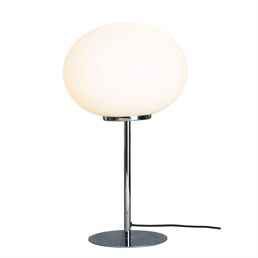 En bordlampe med stor opal glasglobus lyser blødt; den sidder på en slank kromstang med rund kromfod, sort ledning ligger ud til højre på en neutral hvid baggrund.