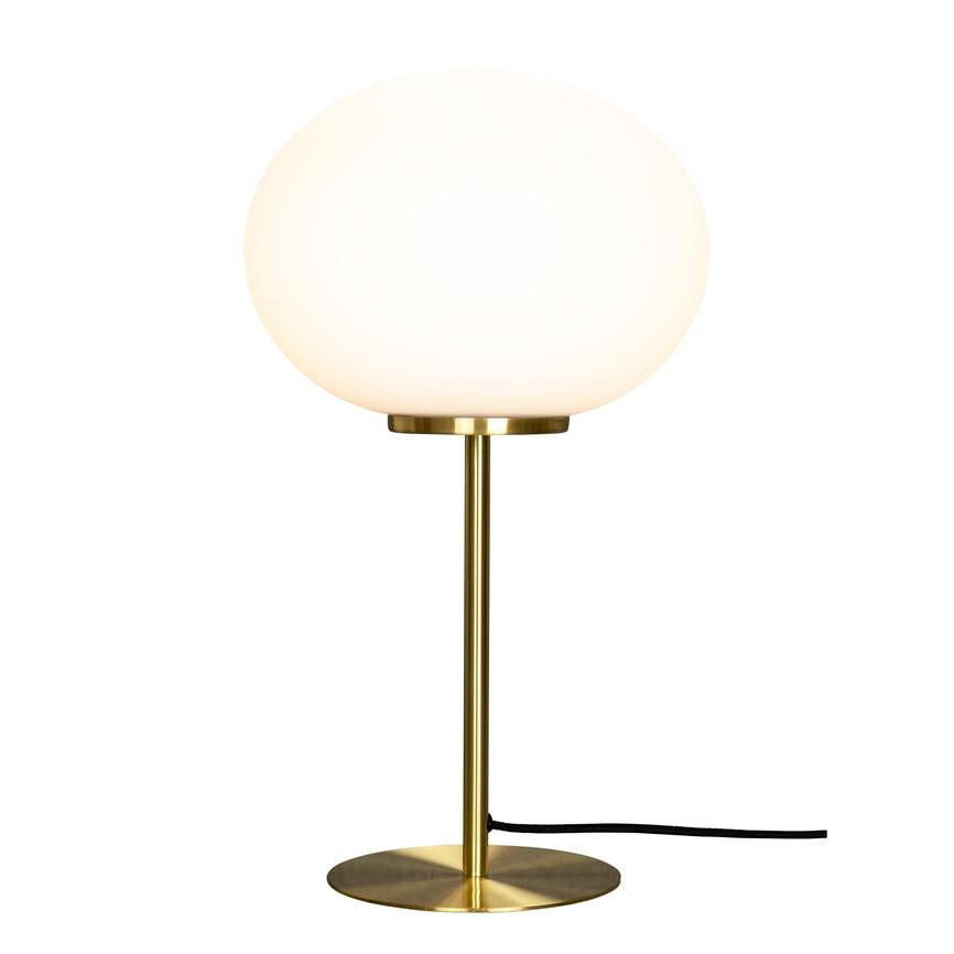 Bordlampe med opal, rund skærm lyser blødt; den er monteret på en slank messingstang og rund messingfod, med en sort strømledning, placeret mod en neutral hvid baggrund.