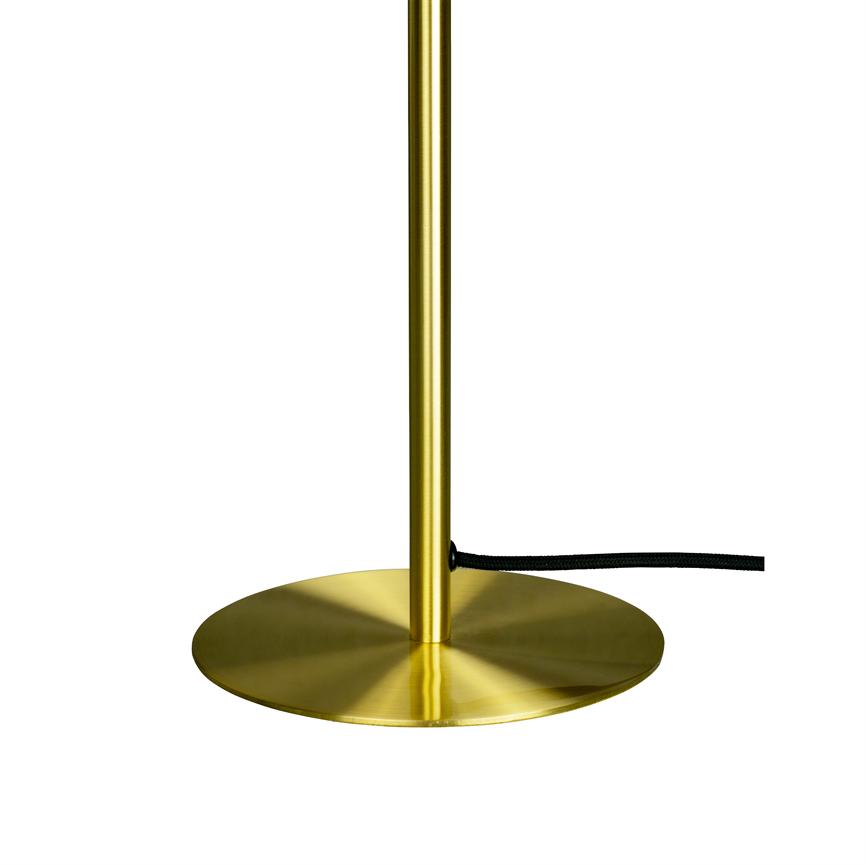 Messingfarvet lampefod med slank stang hviler på en flad, cirkulær bund; en sort tekstilledning løber ud fra stangen mod højre på en hvid baggrund.