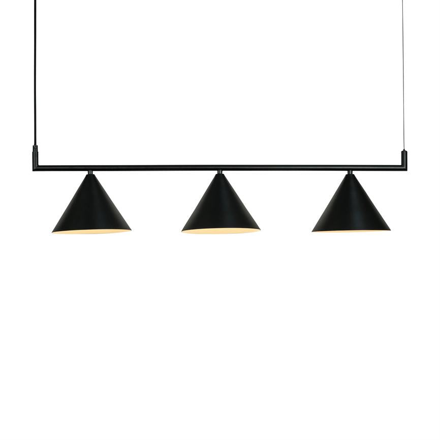 Tre sorte, koniske pendellamper hænger fra en sort stang via tynde kabler, udsender varmt lys, i et rent, hvidt, minimalistisk rum.