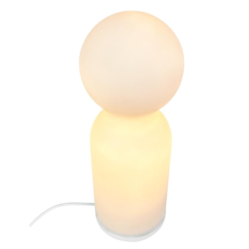 Bordlampe lyser blødt; rund, oplyst kugletop på cylindrisk base, varm hvid glød; står mod en neutral hvid baggrund med synlig hvid strømledning.