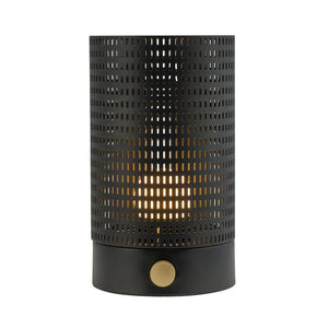 Cylindrisk perforeret bordlampe i sort metal med gylden drejeknap, udsender varmt, priklignende lys gennem rektangulære huller; placeret isoleret mod hvid baggrund.