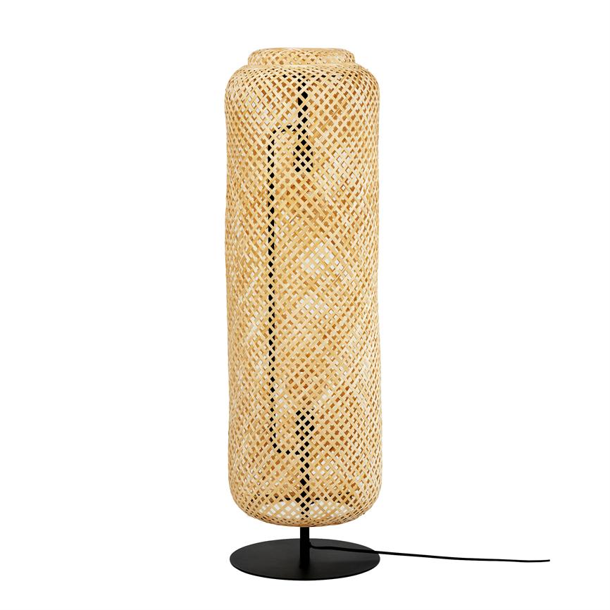Høj, cylindrisk lampe i flettet rattan står på en sort metalfod; vævet skærm omslutter lyskilden, ledning ses på siden, isoleret mod en ren hvid baggrund.