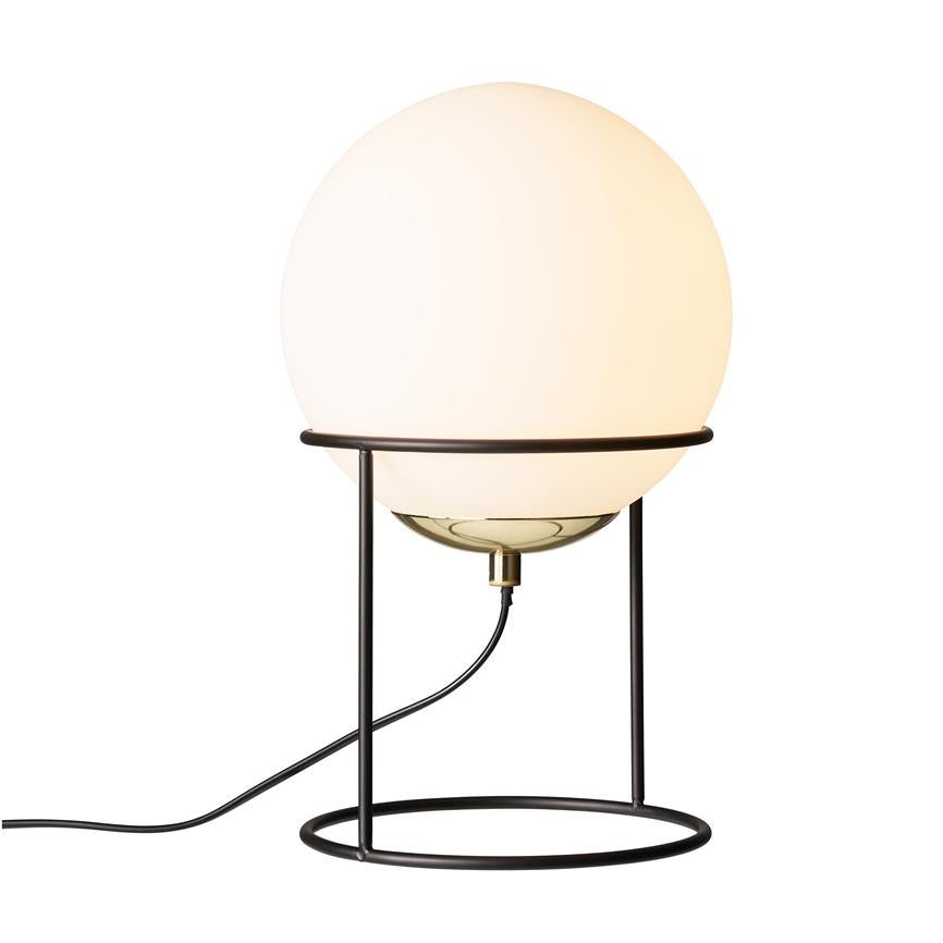 En rund opalhvid glasglob lyser varmt, fæstnet i et sort, åbent metalstativ med cirkulær bund; en sort ledning løber fra lampens underdel mod venstre på hvid baggrund.