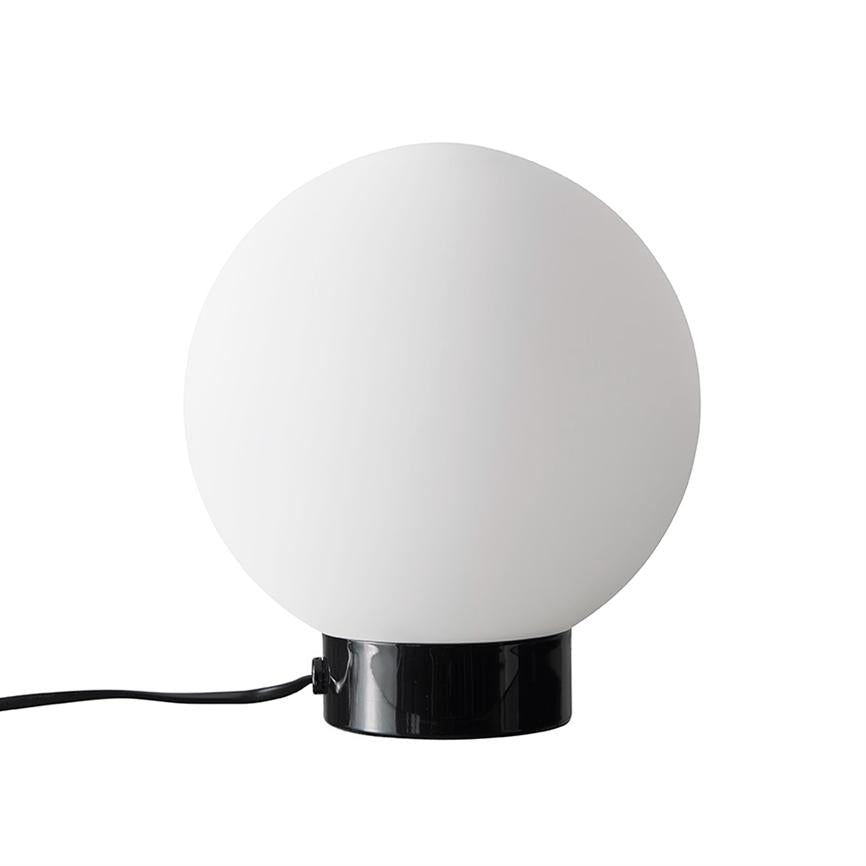 Kuglelampe: en stor hvid glaskugle sidder på en blank sort cylindrisk fod, med en sort ledning som løber ud til siden, placeret mod en neutral hvid baggrund.