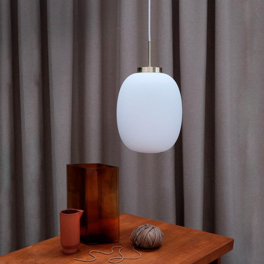 En hvid oval pendel hænger over et træbord; på bordet står en høj brun glasvase, en lille terrakottakop og en garnnøgle med løs snor; baggrunden er grå gardiner.