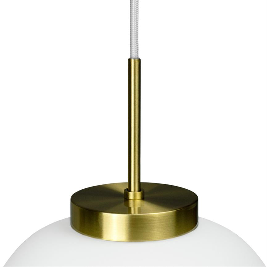 Vedhængslampe hænger fra en hvid tekstilledning; en slank messingstang forbinder en rund messingplade til en mælkehvid glaskuppel på ensfarvet hvid baggrund.