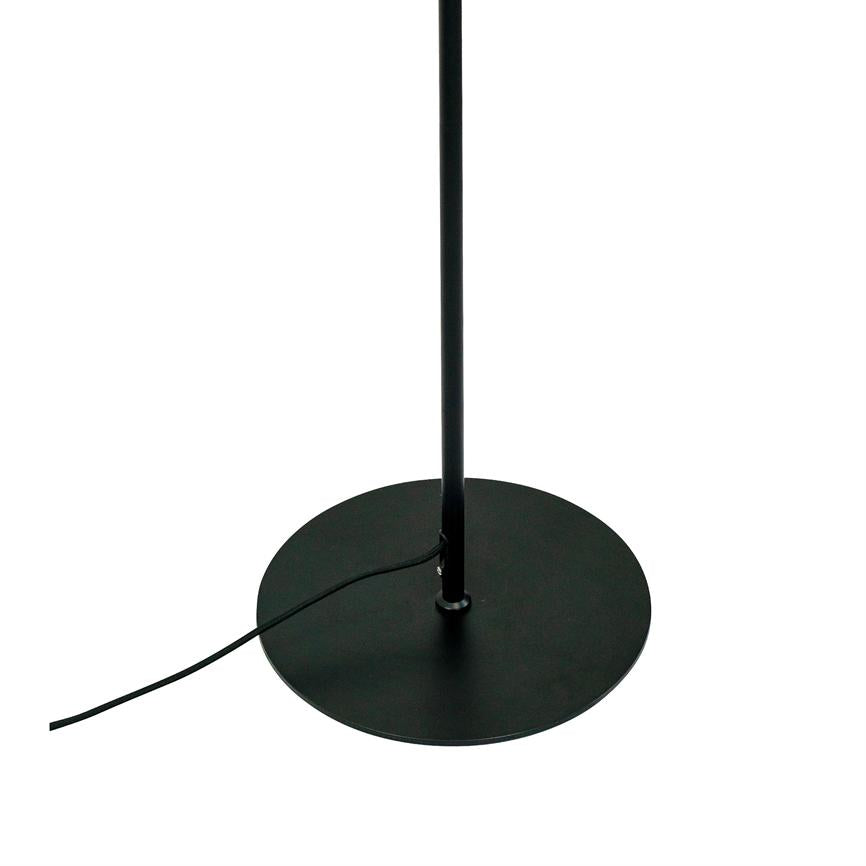 Sort gulvlampe står lodret; dens tynde stolpe er monteret på en rund sort fod, og en sort ledning løber henover bunden på hvid baggrund.
