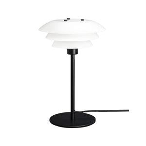 Bordlampe med hvid lagdelt skærm, monteret på slank sort stang; står på rund sort fod og har synlig sort tekstilledning mod hvid baggrund.