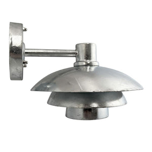 Sølvfarvet metalvæglampe med tre lagdelte, runde skærme er monteret på en kort arm og peger nedad mod en neutral hvid baggrund.