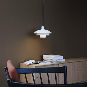 Hvid pendel lampe hænger og kaster blødt lys ned over en lys træskænk med åbne og stablede bøger, foran en mørk væg og en sort stol i forgrunden. 
 Tekst på bogryg: "Giorgio Locatelli Made in Italy"