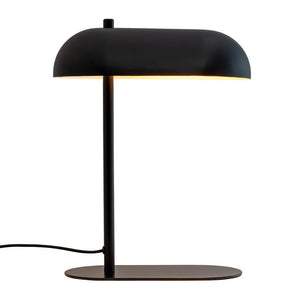 Bordlampe med sort, buet skærm, der udstråler varmt lys nedad; tynd lodret stang forbinder til flad oval metalfod, med strømkabel ud til venstre på hvid baggrund.