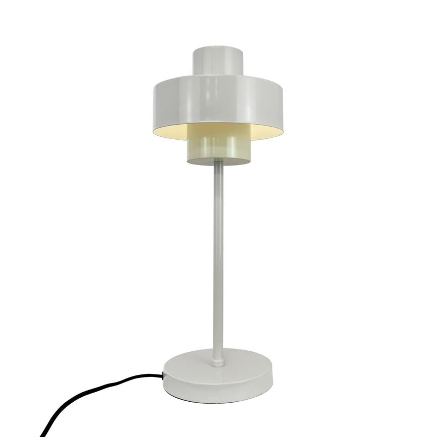 Hvid bordlampe med lagdelte cylindriske skærme står tændt på en slank stang og rund fod; sort ledning løber ud til siden mod en neutral hvid baggrund.