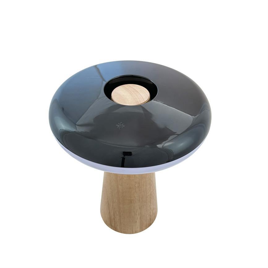 Bordlampe med svampelignende form, blank sort top med centralt rundt indhak og lys træfod; produktfoto på hvid baggrund i lyst studie.