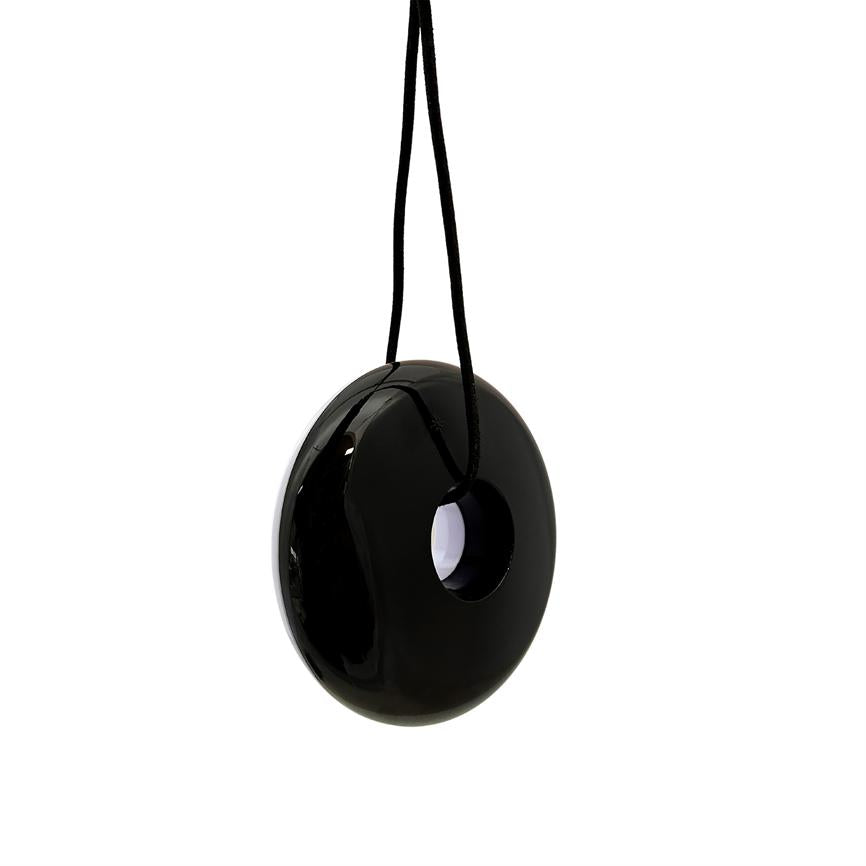 Sort, blank donutformet vedhæng hænger i en sort snor; cirkulært hul i midten; minimalistisk, reflekterende overflade mod en ensartet hvid baggrund.