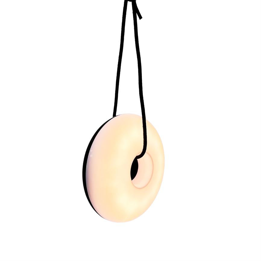 Glaseret, lys pastel-donut hænger i en sort snor, sænket fra toppen og svæver foran en ensartet hvid baggrund.