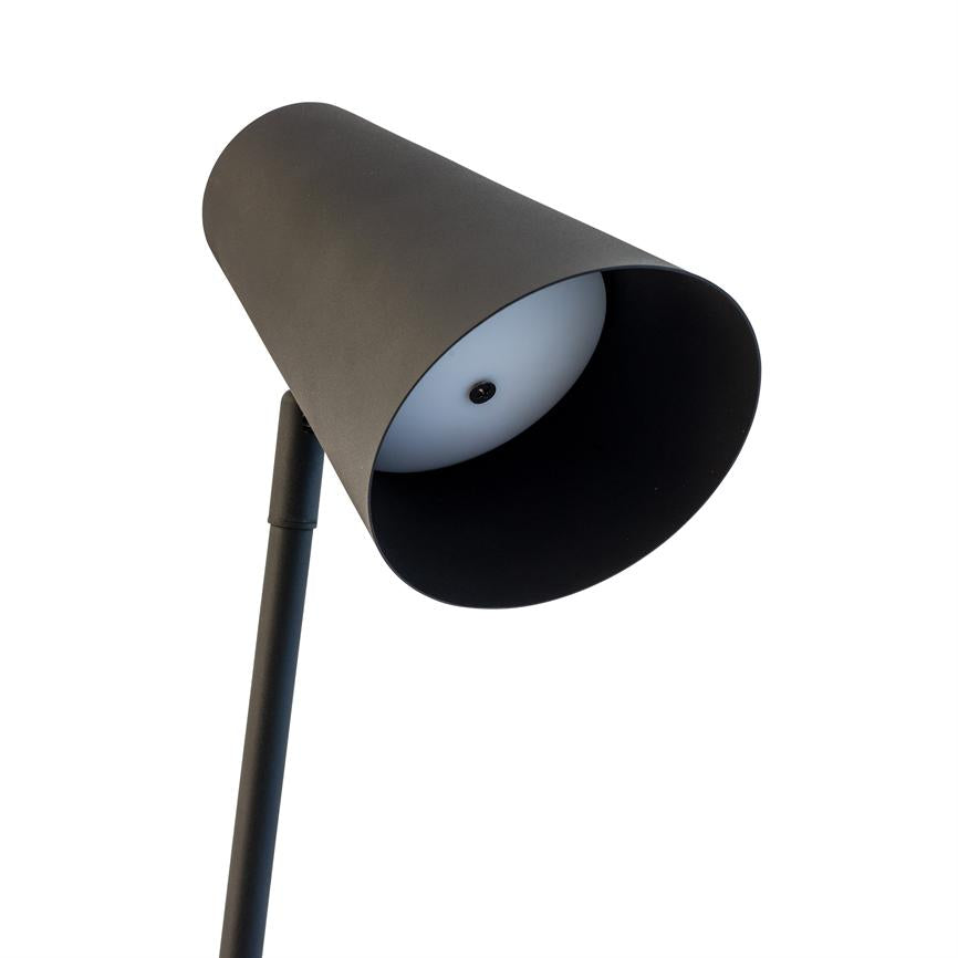 Sort metal lampe med cylindrisk skærm, vendt skråt og peger nedad; hvid indvendig diffusor og slank sort stander på hvid baggrund.