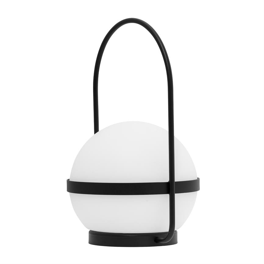 Bærbar kuglelampe holdes af et sort metalbånd og buet hank, hviler på en rund sort base i en lys, neutral studiobaggrund.