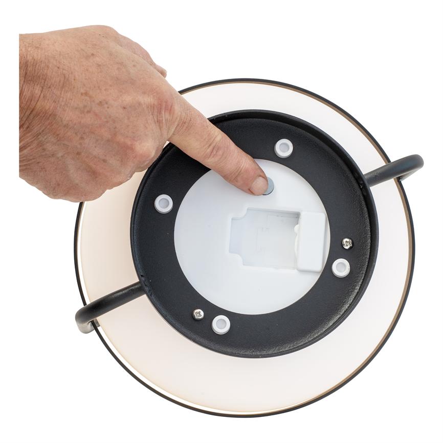 Lampebund (rund) — en finger trykker en lille grå knap på undersiden — omgivet af lampeskærmens kant og en neutral hvid baggrund.