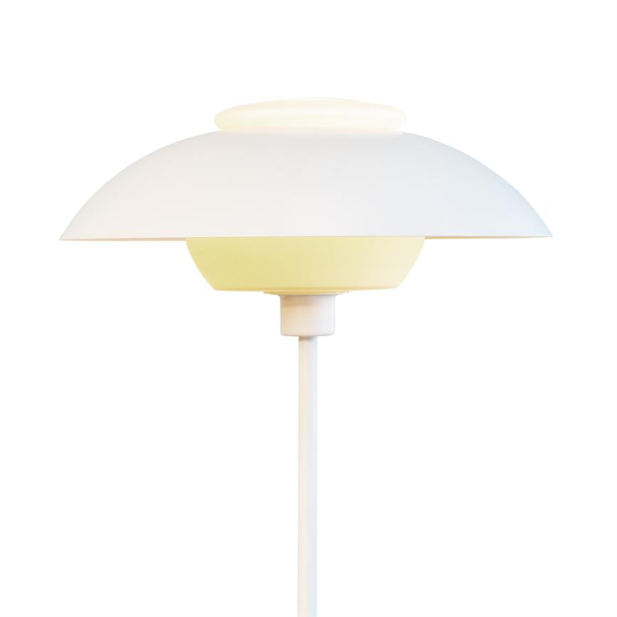 Hvid, rund skærmlampe udsender blødt, varmt og diffust lys på en tynd hvid stander med lagdelt, minimalistisk skærm mod en neutral hvid baggrund.