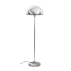 En krom gulvlampe med halvkugleformet skærm står på en slank stang og rund marmorfod; sort ledning ligger løst på hvid baggrund i et tomt, lyst miljø.