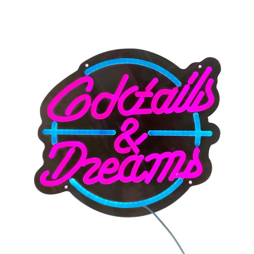 Neonskilt lyser med ordene "Cocktails & Dreams" i pink og blå glasrør, monteret på en sort rund plade med kabel mod hvid baggrund.
 
 Tekst: Cocktails & Dreams